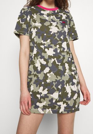 Kvinde iført en grøn, grå og beige camouflage t-shirt kjole med en pink krave og et lille Tommy Jeans-logo på brystet.