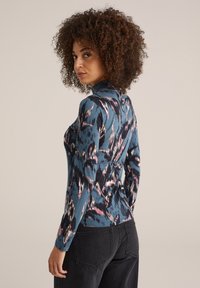 T-shirt à manches longues bleu, arborant un motif abstrait rose et noir. Design col roulé avec une silhouette ajustée et une texture lisse.