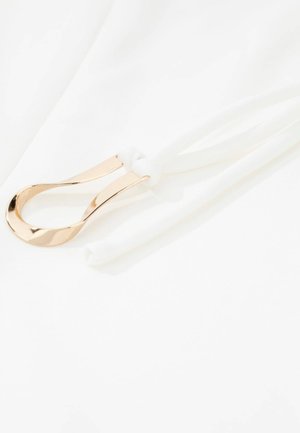 Goldener Metallring mit glatter Oberfläche, befestigt an einem weißen elastischen Band, vor weißem Hintergrund, zeigt sauberes Design und Textur.