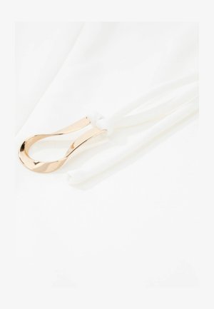 Gouden metalen lus met een gladde afwerking bevestigd aan een wit elastisch bandje, tegen een witte achtergrond, met een strak ontwerp en textuur.