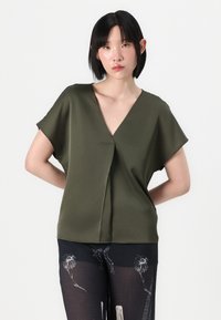 Top corto a maniche corte verde oliva con scollatura a V profonda e dettagli di drappeggio sottili. Tessuto morbido con una vestibilità rilassata, abbinato a pantaloni semitrasparenti con motivo.