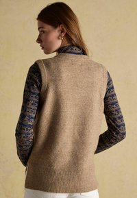 Bež villaest, millel on ribidega äär, kantud üle sinise mustriga särk, millel on kuldsed aktsendid loomade kujunditega.