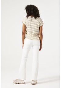Top corto de rayas en beige y crema con pantalones acampanados blancos y zapatillas beige, que muestran un ajuste relajado y una textura suave.