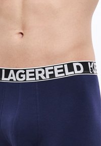 Granatowe bokserki z czarną elastyczną gumą w pasie, na której białymi literami widnieje napis "LAGERFELD". Gładka faktura, dopasowany krój.