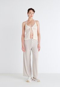 Beige heklet halterneck topp med knyte detalj, paret med løse, stripete vidde-bukser i myke pastellfarger. Modellen står mot en hvit bakgrunn.
