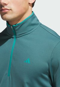 Teal zip-neck pullover, valmistettu teksturoituneesta kankaasta, jossa on kontrastoiva turkoosi vetoketju ja pieni Adidas-logo rinnassa.