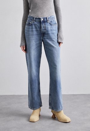 Jeans de mezclilla azul claro de pierna ancha con cintura alta, leve desgastado y cuatro bolsillos. Combinados con zapatos de tacón beige y un top gris de canalé.