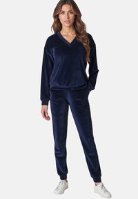 Tuta in velluto blu navy con pullover a V e pantaloni affusolati con polsini elasticizzati. Abbinato a sneakers bianche per un look casual.