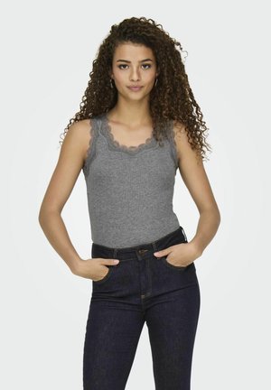 Gray tank top with lace trim at neckline, paired with dark blue high-waisted jeans. Model is standing with hands in pockets.