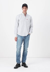 Rutet skjorte i hvit og blå, med en rød logo på brystet; kombinert med lyseblå jeans og svarte dressko.