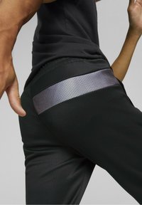 Černé sportovní kalhoty s reflexními stříbrnými síťovanými detaily na zadní kapse. Hladká tkanina s přiléhavým střihem a elastickým pasem.