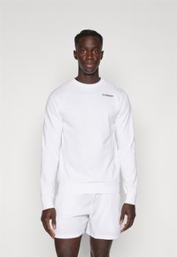Sweatshirt blanc à col rond avec manches longues et poignets côtelés, doté d'un petit logo noir sur la poitrine gauche, associé à un short blanc.