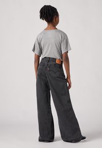 Jeans noirs à jambes larges en denim avec taille haute et coutures contrastées. T-shirt gris à manches courtes, au design simple et à la coupe décontractée.