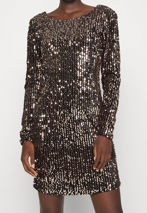 Czarna mini sukienka z długim rękawem, pokryta błyszczącymi ciemnobrązowymi cekinami, noszona przez osobę o ciemnej karnacji, stojącą na tle jednolitego jasnego tła.