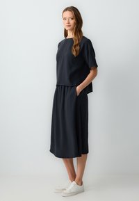 Ensemble deux pièces bleu marine foncé composé d'un haut ample et d'une jupe fluide, tous deux en tissu léger, associés à des baskets blanches.