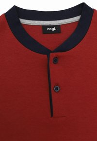 Polo shirt rosso a maniche corte con colletto blu navy, due bottoni e un'etichetta con la scritta "cagi". Tessuto liscio con un design informale.