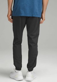 Sorte joggerbukser med elastiske manchetter, glat tekstur, sidelommer, sammen med hvide kondisko. T-shirten er blå og har rund hals.