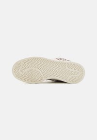Shoe sole with zigzag and curved tread patterns, light beige color, leopard print upper partially visible on white background.