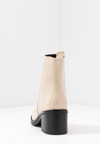 Bottes chelsea en cuir beige avec des panneaux latéraux élastiqués, un bout rond et un talon bloc texturé noir. Les coutures mettent en valeur le design.