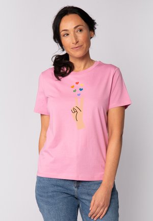 T-shirt en coton rose avec un graphique d'une main faisant un signe de paix, surmonté de cœurs colorés. Coupe décontractée avec des manches courtes et un col rond.