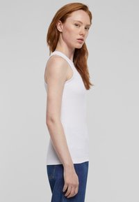 Bílý tílko vyrobené z bavlny, se slim fit střihem, širokými ramínky a kulatým výstřihem. Design je jednoduchý bez viditelných vzorů.