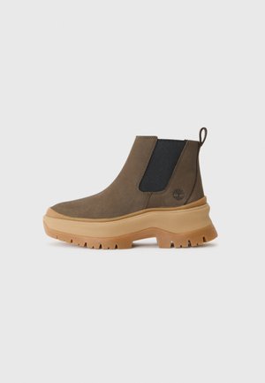 Brown suede ankle boots with elastic side panels and a chunky gum rubber sole. Features a pull tab and embossed logo on the side.