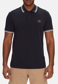 Polo shirt blu navy con strisce bianche a contrasto sul colletto e sulle maniche. Presenta un piccolo logo rotondo sul petto. Realizzato in cotone.