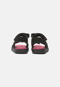 Mustat sandaalit säädettävillä hihnoilla ja pehmeällä vaaleanpunaisella sisäpohjalla. Kumipohja, jossa on uritettu kuvio pitävyydelle, avoin takasuunnittelu.