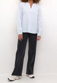 Ljusblå blus med lång ärm, vertikala ränder och delad halsringning, tillsammans med mörkgrå vida jeans och vita sneakers.