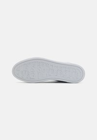 Suola bianca di sneaker con motivo in rilievo del logo "GUESS" e bordi texturizzati. Materiale liscio con punta arrotondata e profilo piatto.