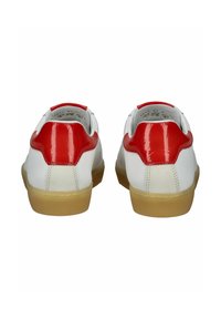 Bílé tenisky s červenými lesklými akcenty na patách, gumovými podrážkami a polstrovanými límci. Hladké a texturované povrchy s kontrastními barevnými detaily.