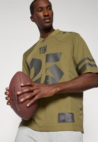 Olivově zelený dres NFL s černými čísly "25" a logem, krátké rukávy, síťová textura a nášivka s brandingem NFL na lemu.
