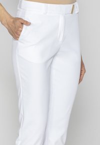 Białe dopasowane spodnie wykonane z gładkiego materiału. Posiadają płaski przód, boczne kieszenie oraz akcent w postaci złotej klamry paska.