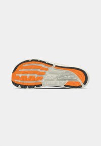 Sole of a running shoe, featuring a textured design in black and orange rubber, with grooves for traction and a detailed patterned surface.