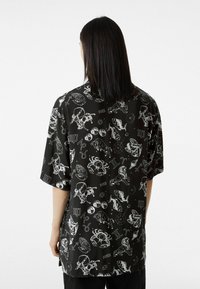 Camiseta negra de manga corta con un estampado blanco de temática astrológica que muestra símbolos e íconos del zodíaco en toda la tela.