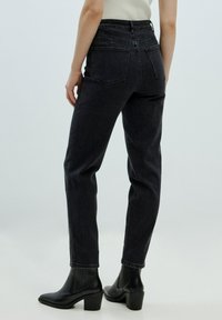 Schwarze, hochgeschnittene Jeans aus Denim mit schmal zulaufendem Bein, ausgestattet mit zwei Gesäßtaschen und umgeschlagenen Saumabschlüssen, kombiniert mit schwarzen, hochhackigen Stiefeletten.