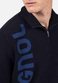 Dunkelblauer Pullover mit halbem Reißverschluss, aus Strickstoff. Besitzt ein großes, strukturiertes, kontrastierendes Logo auf der linken Seite.