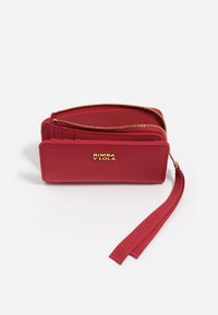 Raudonas audinys užtrauktuku užtraukiamas piniginė su auksiniu Bimba y Lola logotipu, kelių kortelių lizdais ir prisegamu riešo dirželiu baltoje fone.