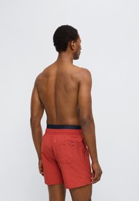 Κόκκινα μαγιό σορτς με μπλε ελαστική μέση, διαθέτουν πίσω τσέπη και λεπτομέρεια με θηλιά. Ελαφρύ ύφασμα με λεία υφή.