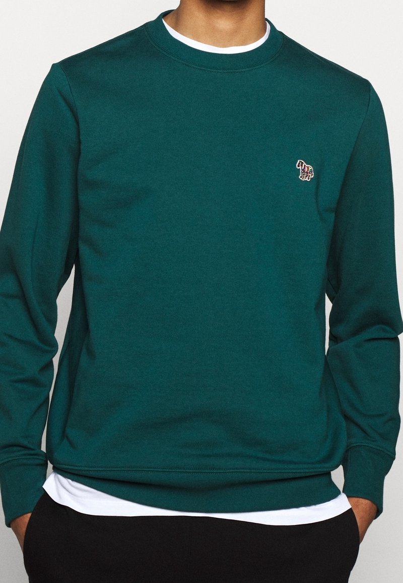 Sweatshirt vert à col rond fabriqué en tissu doux. Il présente des poignets et un ourlet côtelés, avec un petit design brodé sur la poitrine.