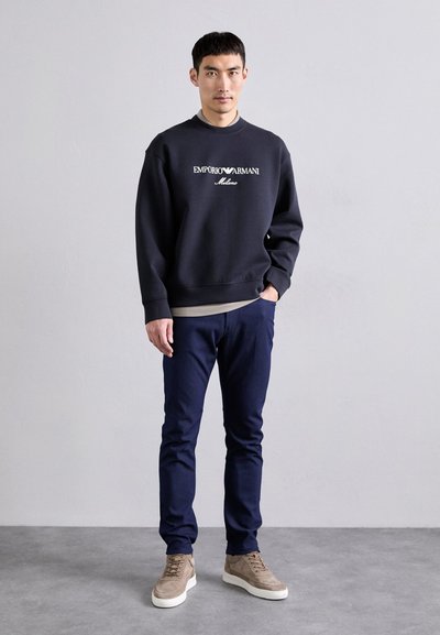 Sweat-shirt marine avec le texte blanc "Emporio Armani Milano", associé à un pantalon bleu foncé et des baskets montantes marron clair. Texture lisse.
