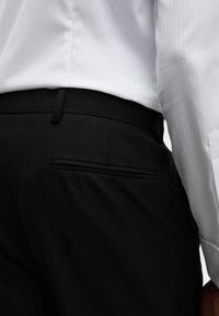 Czarne formalne spodnie o gładkiej fakturze, z jedną tylnią kieszenią i paskiem, zestawione z białą koszulą w prążki.