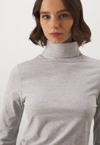 Hele hall, keha ümber liibuv turtleneck-särgi top, mis on valmistatud pehmest ja tekstureeritud kangast, pikaaegsete varrukatega ja kõrge kaelusega disain, sobib ideaalselt kihitamiseks.