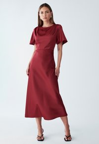 Burgundska satenasta obleka s kratkimi rokavi, okroglo izrezom, prilegajočim zgornjim delom in kapljično krilo, ki se ponaša z gladko teksturo in elegantno silhueto.