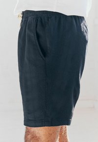 Pantalones cortos negros y texturizados con cintura elástica y bolsillos laterales. Diseño sencillo, de largo hasta la rodilla con un detalle en la costura lateral.