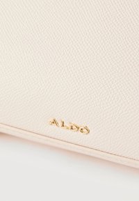 Gros plan sur une surface en cuir beige texturé avec un petit logo doré ALDO en bas au centre.