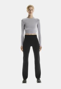 Hellgraues langärmeliges Crop-Top, kombiniert mit hochgeschnittenen schwarzen Hosen, beide aus glattem, dehnbarem Material; neutrale Sport-Schuhe.
