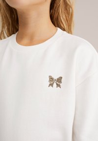 Witte sweatshirt met een ronde hals en een subtiele gouden geborduurde strik op de linkerborst. Zachte stof met een gladde textuur.