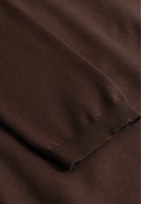 Hnědá pletená látka v detailu zobrazující složený rukáv s žebrovaným lemem manžety.