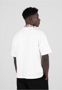 Valge puuvillane t-särk lillemustriga kraega. Lühikesed varrukad, mugav lõige ja sirge serv. Ei ole nähtavat brändimist.